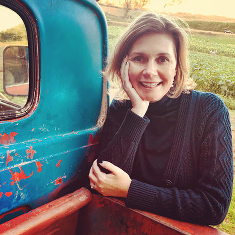 A woman leaning on the back of an old truck.