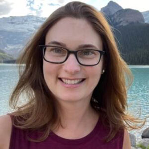 A woman with glasses standing in front of a body of water.