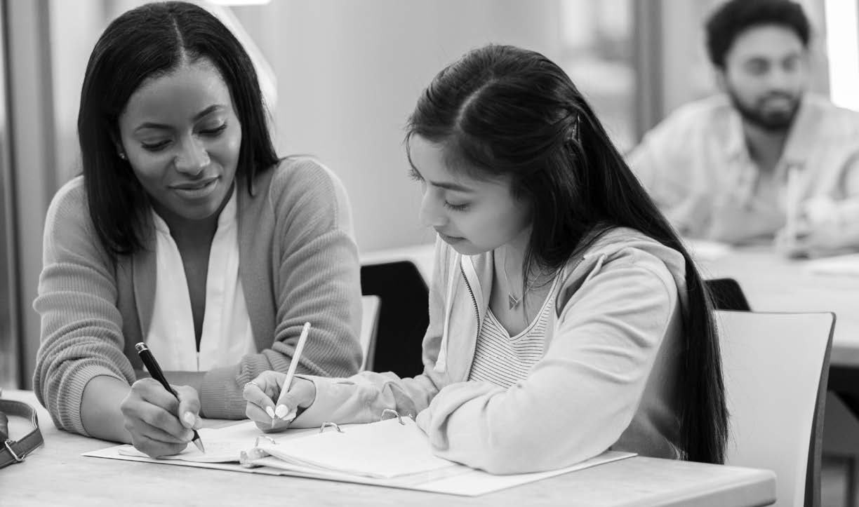 Two women sitting at a table writing on paper.