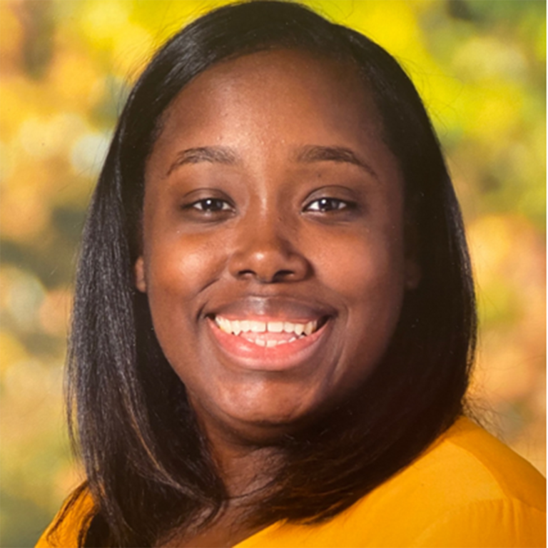 A woman in an orange shirt smiling for the camera.